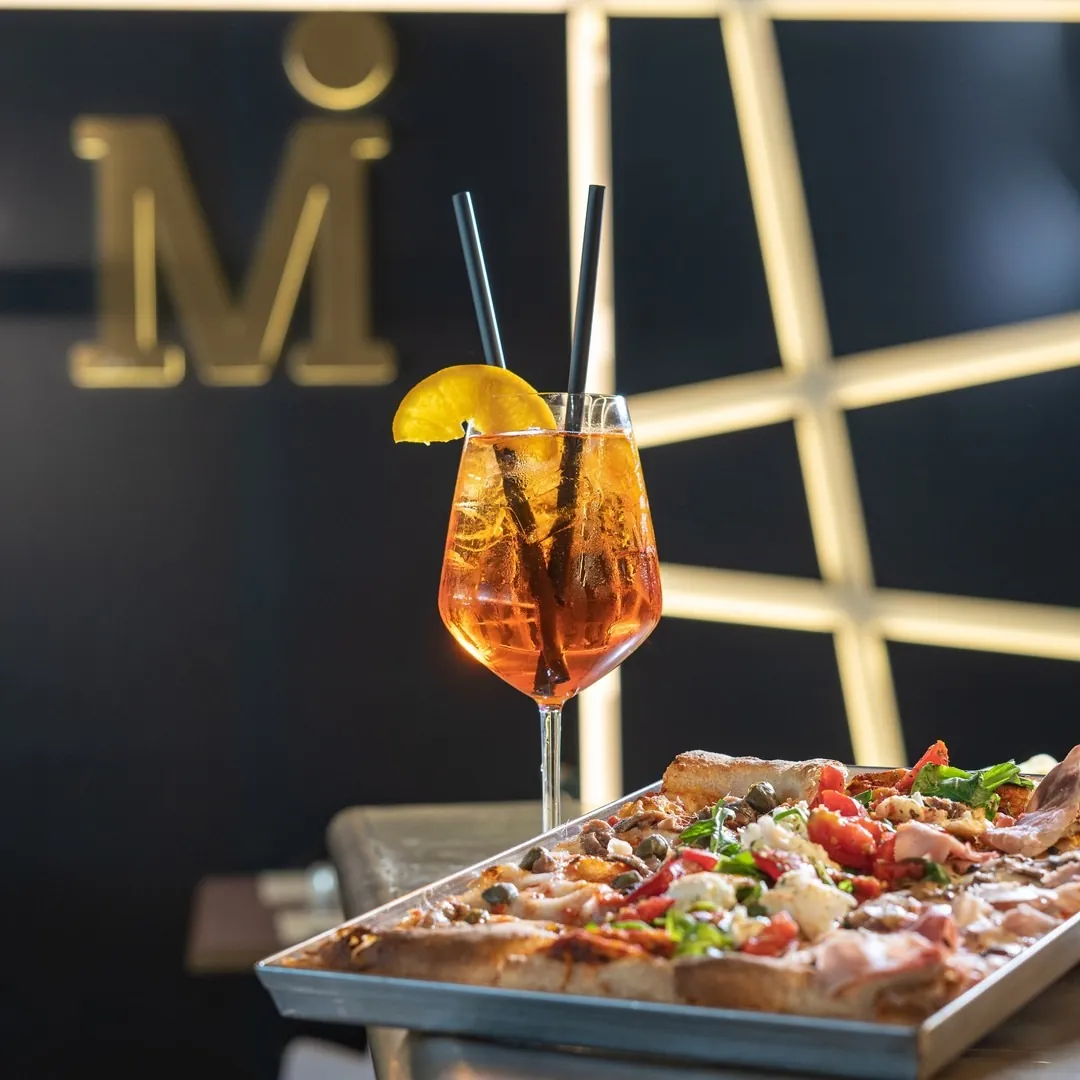 Spritz e pizza serviti davanti alla 'M' dorata del locale